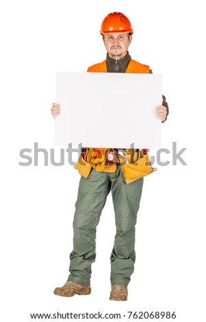 male builder or manual worker in helmet with white blank banner over white wall background. repair, construction, building, people and maintenance concept