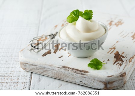 Traditional mayonnaise sauce in white ceramic bowl and ingredients for its preparation on white wooden background. Selective focus. Royalty-Free Stock Photo #762086551