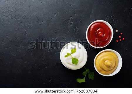 Set of three sauces - mayonnaise, mustard and ketchup in white ceramic bowls on  black stone or concrete background. Selective focus. Top view. Royalty-Free Stock Photo #762087034