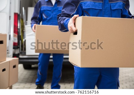 Close-up Of Two Mover's Hand In Uniform Carrying Cardboard Box Royalty-Free Stock Photo #762116716