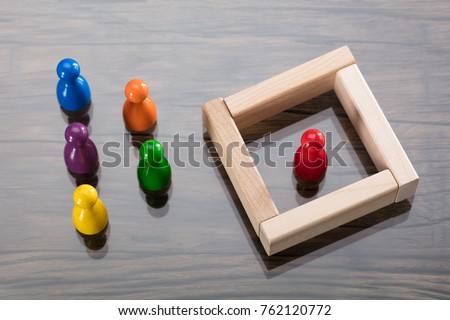 Red Figurine Pawn Separated By Wooden Blocks From Colorful Figurines Royalty-Free Stock Photo #762120772