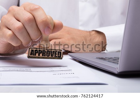 Close-up Of A Person's Hand Stamping With Approved Stamp On Document At Desk Royalty-Free Stock Photo #762124417
