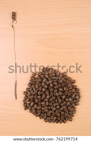 Fishing bait with hook and brown pre-drilled halibut pellets for carp fishing isolated on wood background with soft shadow