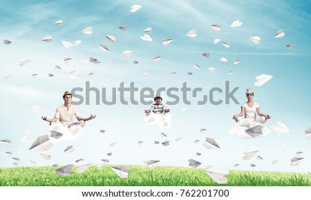Young family keeping eyes closed and looking concentrated while meditating on clouds among flying paper planes with bright and beautiful landscape on background.