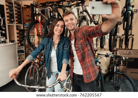 A young guy and a girl make a selfie at a bike store. They came here to buy a new bike. The girl holding the handlebars.