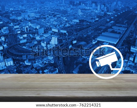 cctv camera icon on wooden table over modern city tower, street and expressway, Business security concept