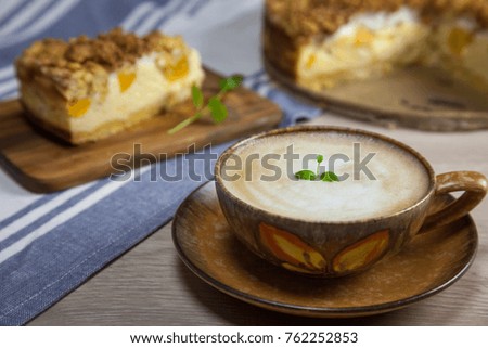 Cup of coffee with the slice of cheesecake with peach on the wooden cutting board and cake on the background