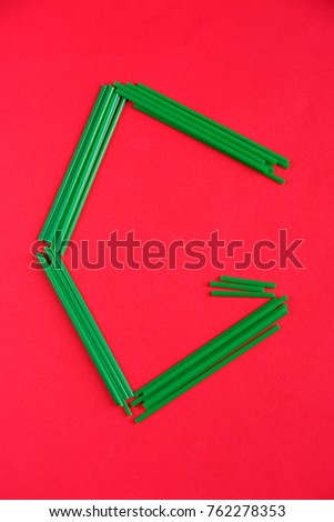 The letter G of green color, is laid out of cocktail tubes on a red background.