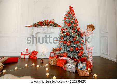 Little boy in elegant pajamas decorates a Christmas tree