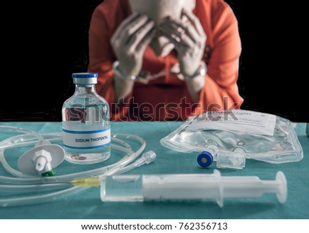 Prisoner handcuffed to death by lethal injection, vial with sodium thiopental and syringe on top of a table, conceptual image Royalty-Free Stock Photo #762356713