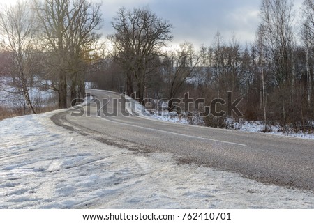 country road in winter with tyre tracks in the snow and ice