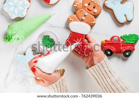 Preparation for Christmas, the girl (hands in the picture) decorates homemade hand-made traditional gingerbread with multicolored sugar icing, biscuits, white marble table. top view copy space