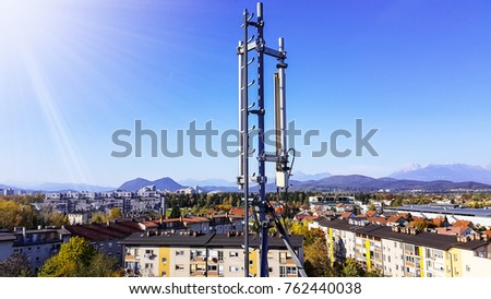 Mobile telecommunication cellular radio network antennas on a mast on the roof broadcasting signal waves over the city on a clear sunny day with blue sky and clouds