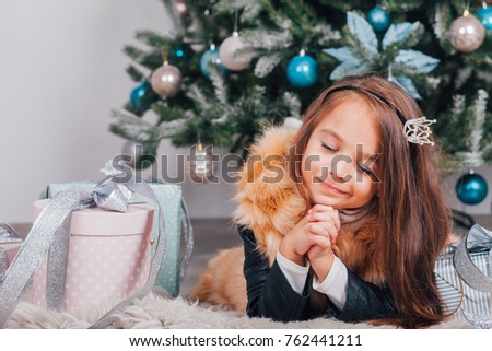 Beautiful happy girl christmas room interior. Female child open Xmas gift near decorated fir tree and fireplace. Winter holidays concept
