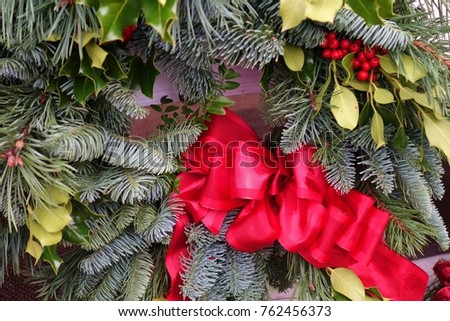 Beautiful colorful extreme closeup of a Christmas wreath with holiday leaves, pine needles, mistletoe and a bright red ribbon tied in a large bow.