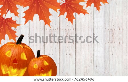 Autumn carved pumpkin pumpkin with yellow leaves on a wooden background
