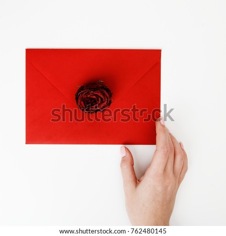 Minimalist fashion and beauty photo. A love letter in a red envelope with a rose. Female hands holding a love letter. The concept of St. Valentine's Day. Romantic photography. 14 february. Flat lay