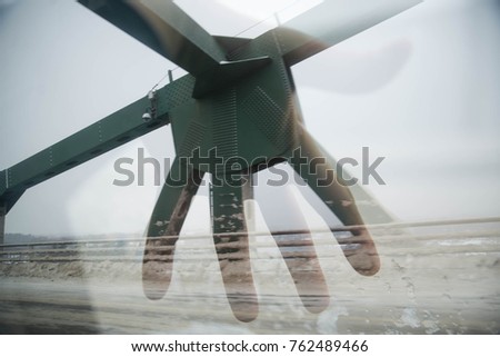 A double-exposure of a hand and the metal beams of a bridge. 