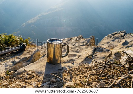 A metal mug stands on the edge of the cliff, against the background of high mountains, in the rays of the sun