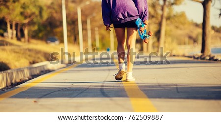 a girl with slender legs in a purple jacket walks along the road holding a skateboard in her hand, a longboard