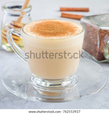 Healthy rooibos red tea latte topped with cinnamon, in glass cup and ingredients on background, square