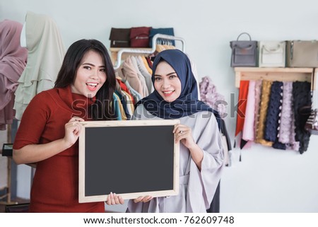 portrait of two asian fashion store owner smiling while holding blank board sign in her shop
