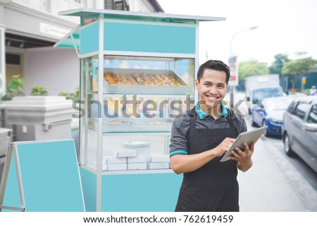 happy male entrepreneur with his newly open small business food stall. promoting online using tablet pc Royalty-Free Stock Photo #762619459