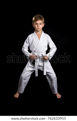 Ready front pose with lowered clenched fists. Kid in brand new white kimono on the black background