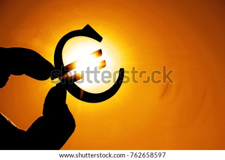 man's hand hold the Euro icon silhouette against sunny orange golden and yellow sky. sun rays. euro sign, symbol of money, idea of Euro Union, sun rays beam