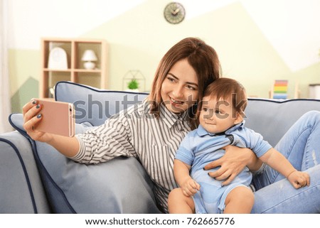 Mother with baby boy taking selfie on sofa at home