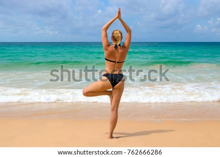Beautiful young woman is doing yoga near the sea tree pose.