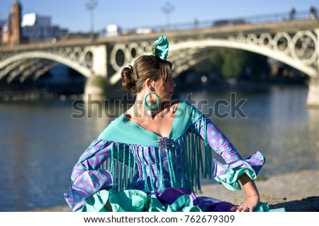 The woman from the traditional flamenco green dress is sitting at the edge of the Guadalquivir