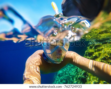 Underwater close surface split photo of a young playful man with a snorkelling mask swimming in the turquoise exotic sea for summer vacation.