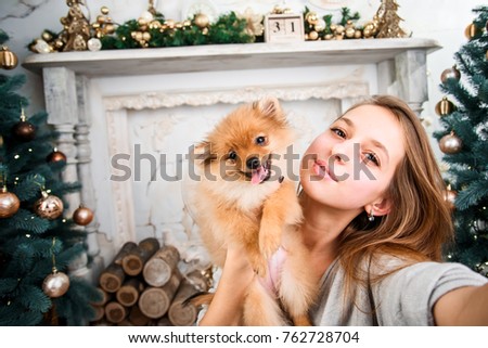 Young girl making a selfie with a cute pomeranian dog on Christmas background. Christmas celebration. 
