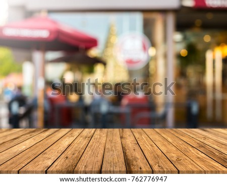 Picture of a brown wood table in front of a cafe. Blurred background with bokeh lights.