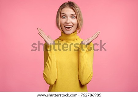 Excited beautiful young female gestures, has amazd and happy expression, didn`t expect to recieve present from friend, expresses positiveness and unexpectedness. People and body language concept