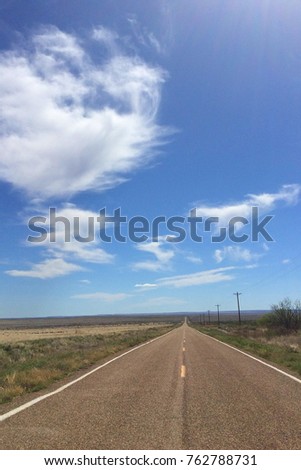 Portrait picture of a road stretching on for miles on a sunny day with blue sky, captured on the New Mexico and Texas state line in USA