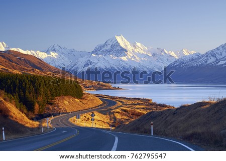 Scenic winding road along Lake Pukaki to Mount Cook National Park, South Island, New Zealand during cold and windy winter morning. Most beautiful view of Mount Cook. Royalty-Free Stock Photo #762795547