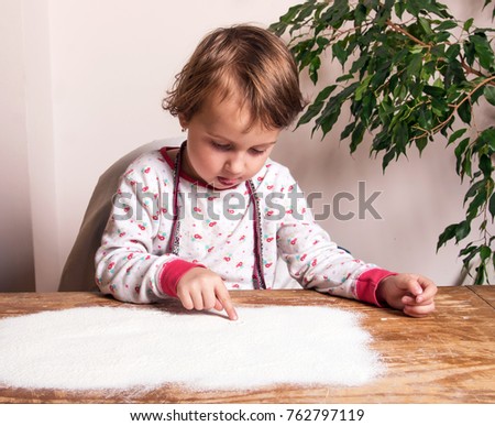 Beautiful little girl draws on a board with scattered flour (creativity, upbringing, relaxation, antistress - concept)