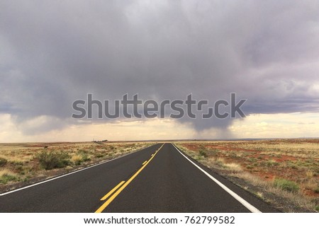 Landscape picture of a road stretching on for miles with storm cloud in a distance near Winslow, Arizona, USA