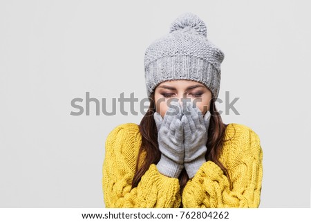 Young woman has cold and cough, portrait of a sick girl wearing warm clothing, isolated on gray background