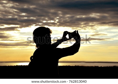 Man silhouette using a smartphone to take pictures sunset.