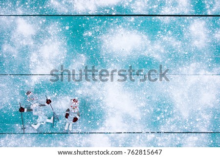 Two athletes ornaments on snow covered antique teal blue wood background; blank winter sign with white copy space