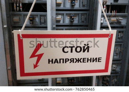 White prohibiting sign "Stop, voltage" against the background of electrical equipment. Translation of the inscription from the Russian language.