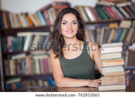 Beautiful young female student sitting on the background of bookshelves in the library
