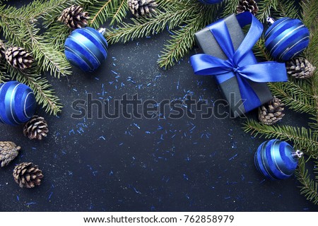 Christmas gift with blue ribbon and blue balls, tree branches and cones on dark blue background with copy space. Royalty-Free Stock Photo #762858979