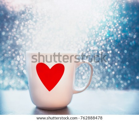 Mug with red heart and bokeh at blue background, close up, front view. Layout of greeting card for Mothers day, Valentines day or birthday. Love concept