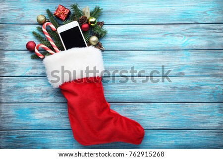 Red stocking with fir-tree branches and smartphone on wooden table