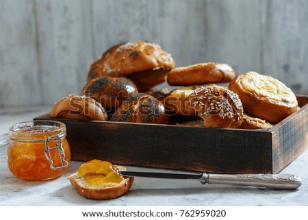 Wooden tray with buns and a jar of orange marmalade for Breakfast at the old kitchen table.