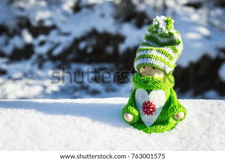 Toy wooden girl in Scandinavian style in knitted green clothes in the snow. Christmas toys